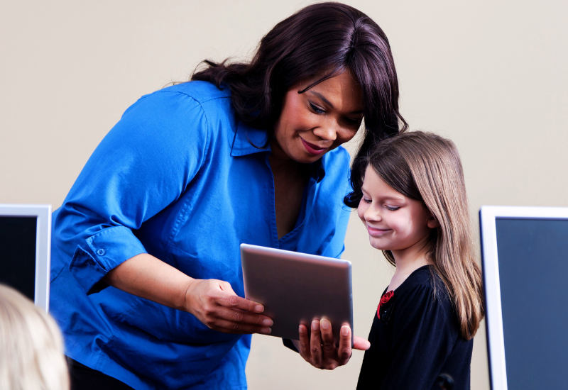 A teacher and a little girl looking at a tablet
