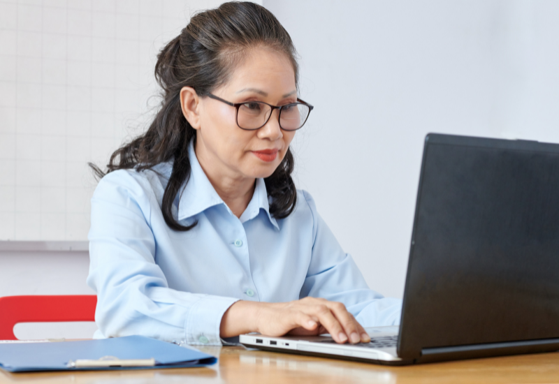 A woman in glasses is using a laptop in an office.
