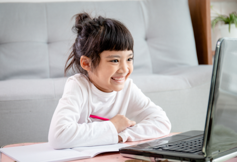 Young student smiles at laptop, sitting on the floor
