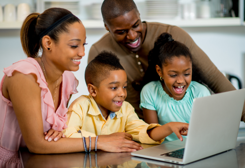 Family uses laptop together, smiling
