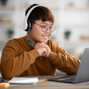 Middle school student with his hands clasped, wearing headphones, looks at laptop and smiles