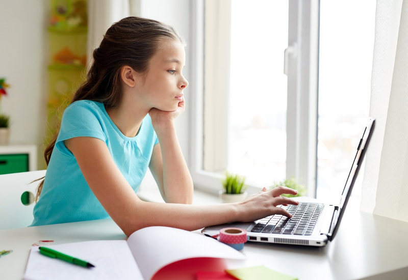 Girl works on laptop near a bright window
