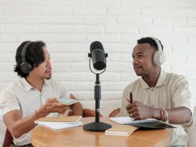 Two people with a microphone between them, sitting down and recording a podcast
