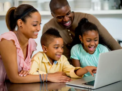 Family uses laptop together, smiling
