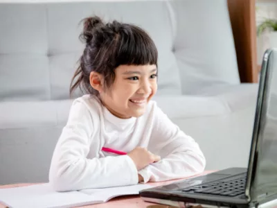 Young student smiles at laptop, sitting on the floor
