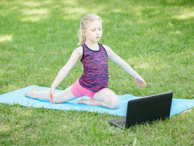Student exercises on yoga mat outside in front of laptop
