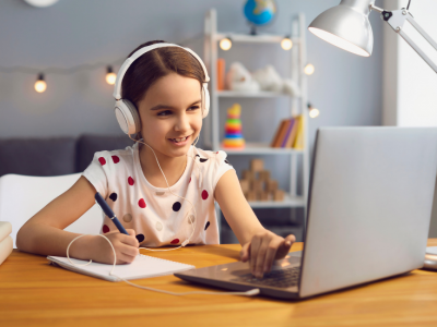 Young girl sits in bedroom, working on laptop, listening to audio over headphones

