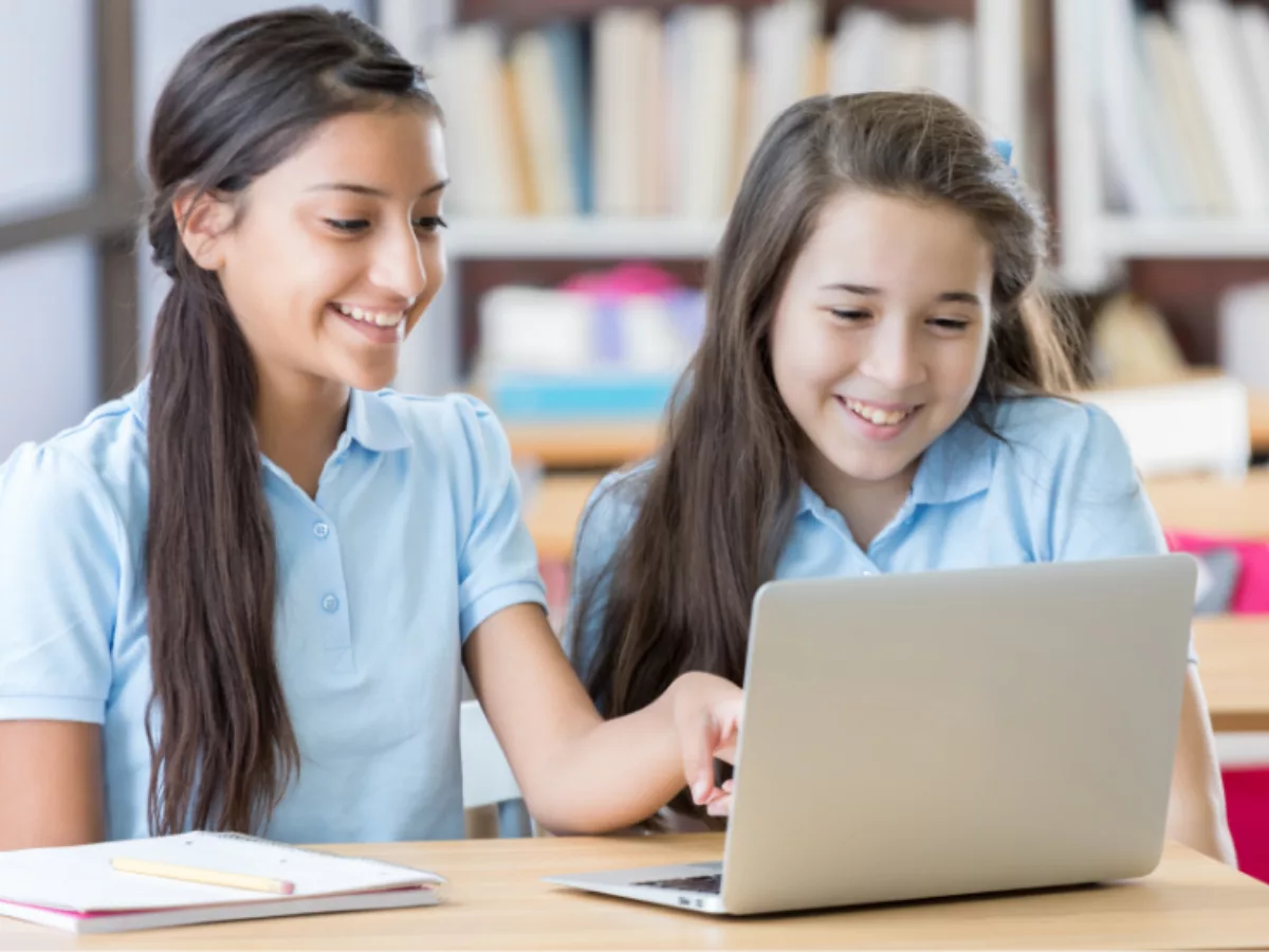 Two young girls sitting at a table using a laptop
