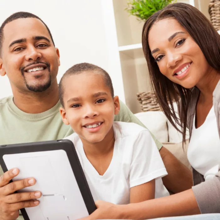 A child and his parents look at camera, smiling, while holding a tablet