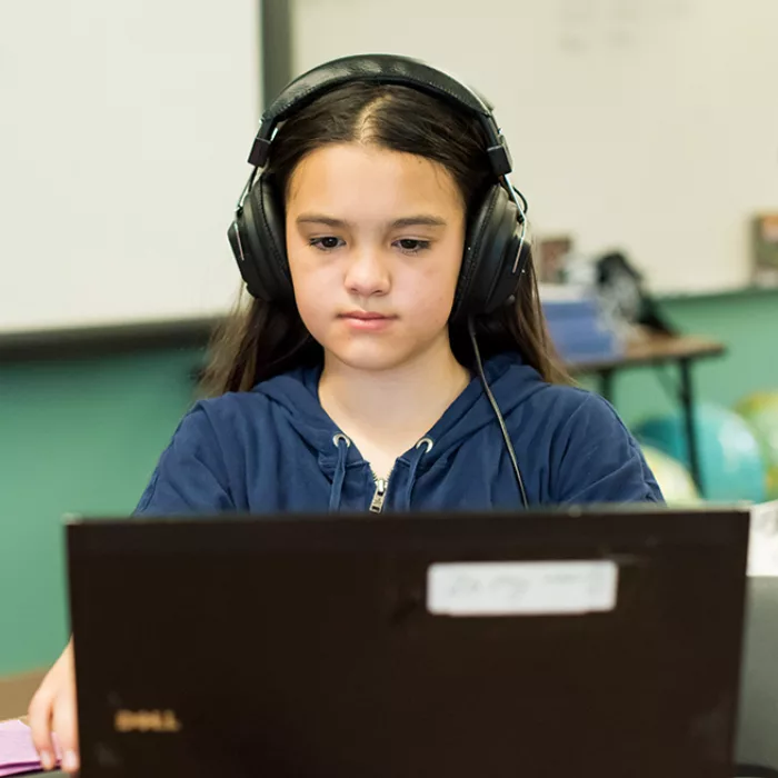 Student looks down at laptop, wearing headphones, smiling
