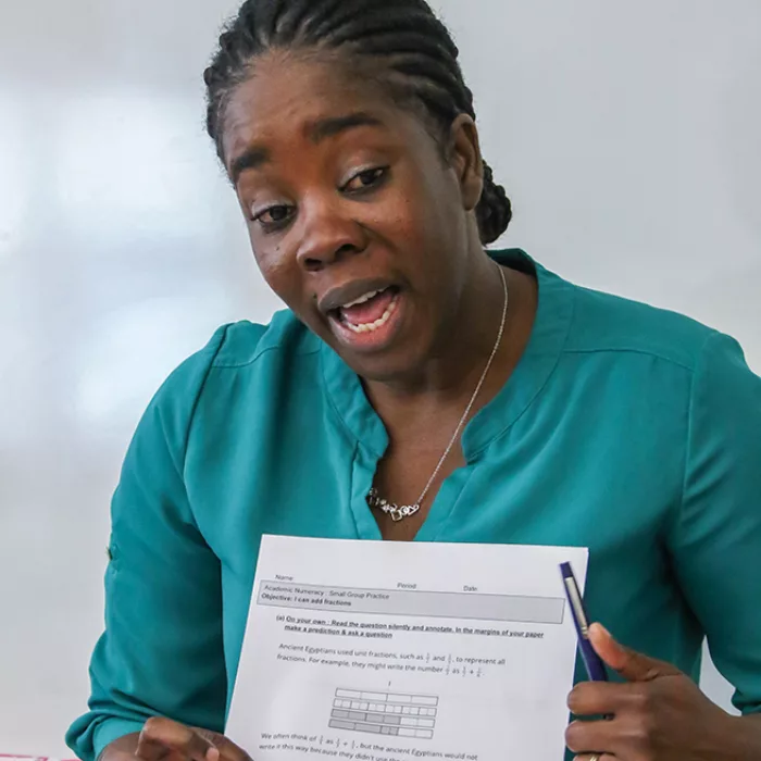 Teacher holds up paper as she speaks to room

