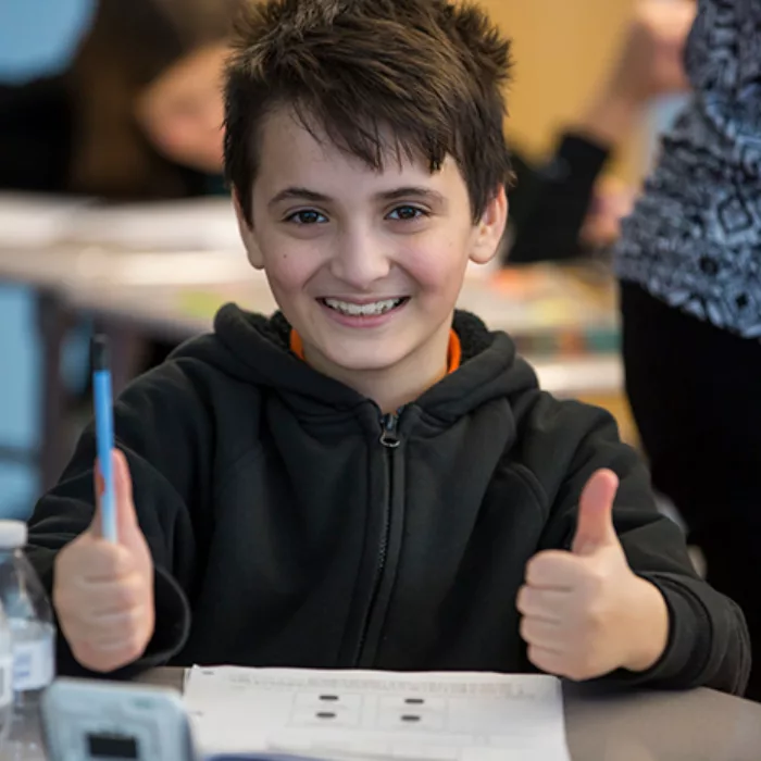 Student sitting at desk gives two thumbs up, smiling