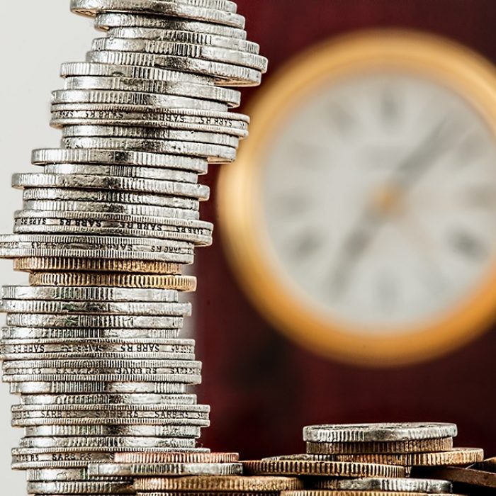 Stack of coins with blurred clock in background
