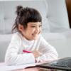 Young student smiles at laptop, sitting on the floor