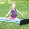 Student exercises on yoga mat outside in front of laptop
