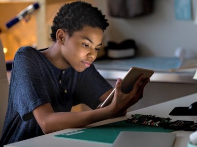 Boy looks at tablet screen, sitting at desk
