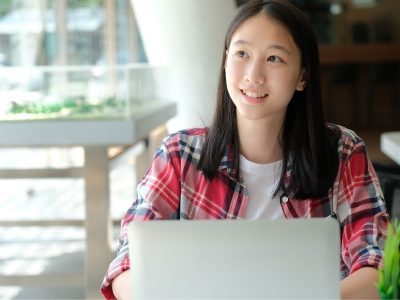 Girl looks upward, smiling, sitting in front of laptop
