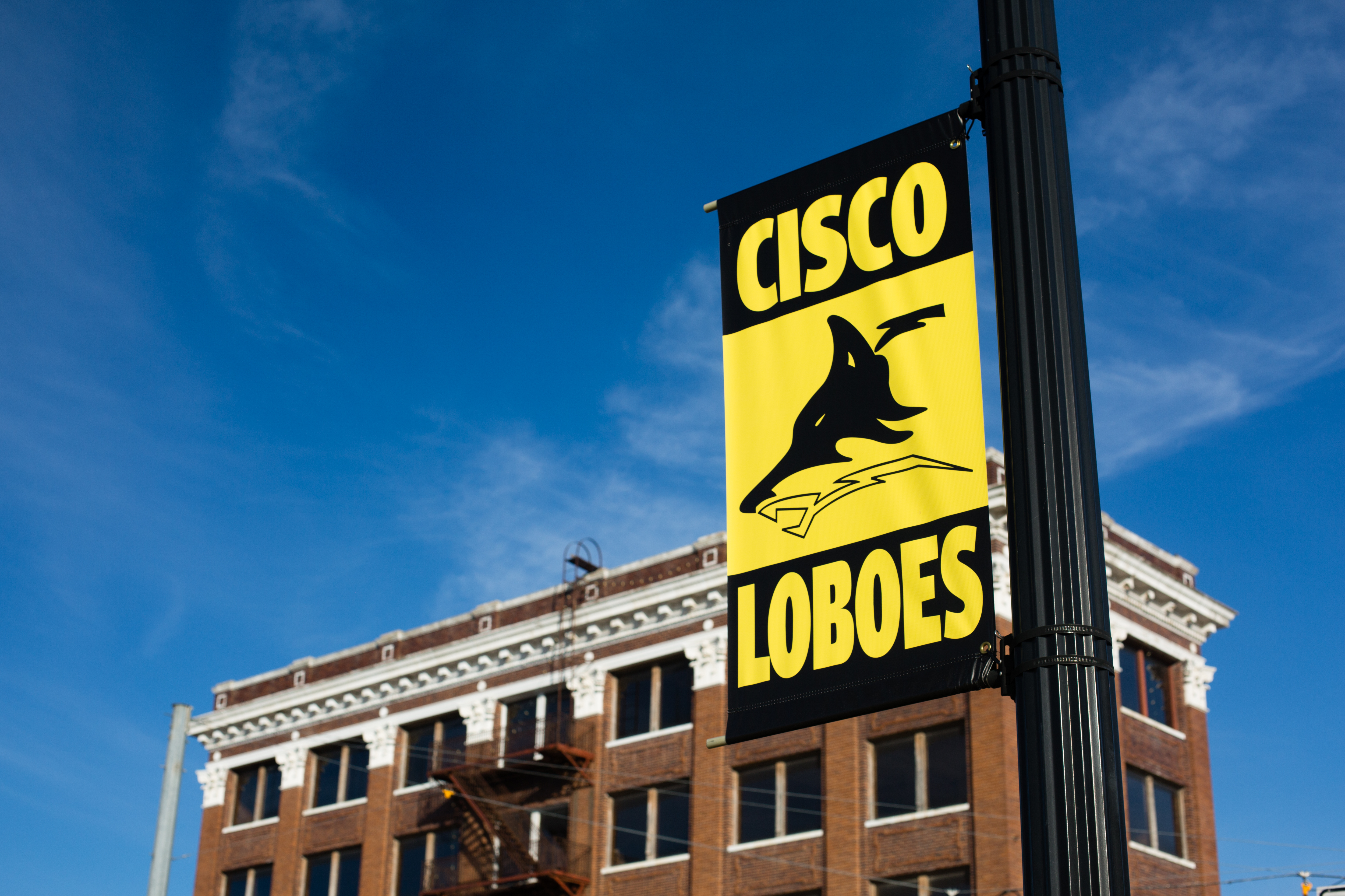 Outdoor view of school building, with a yellow and black sign reading "Cisco Loboes" in the foreground, showing the school's mascot
