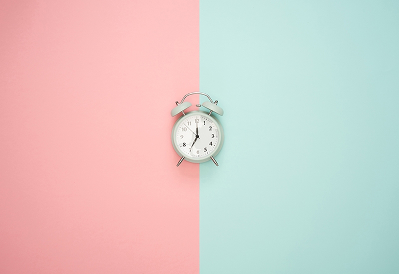 Alarm clock sitting on top of a two-toned pink and turquoise background
