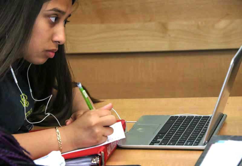 Photo of student working on her laptop and writing by hand