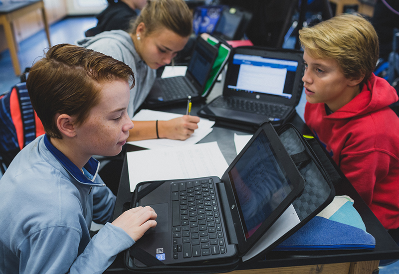 Three students working together while using laptops

