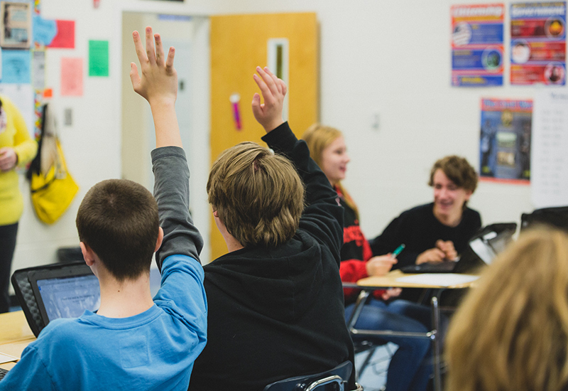 Two students raise their hands while sitting in classroom