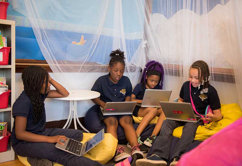 Four female students sit on floor, bean bag chairs while working on laptops