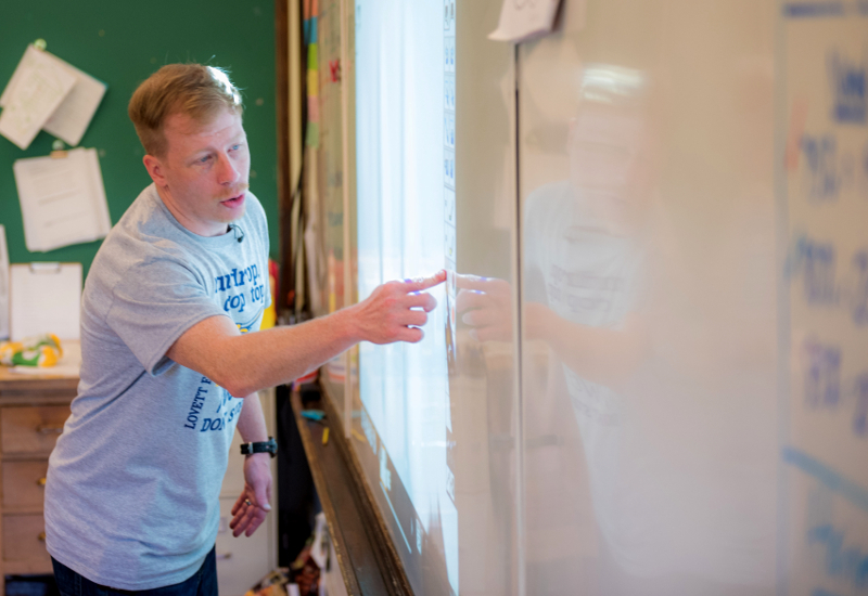 Teacher stands in front of interactive white board, pointing at the screen
