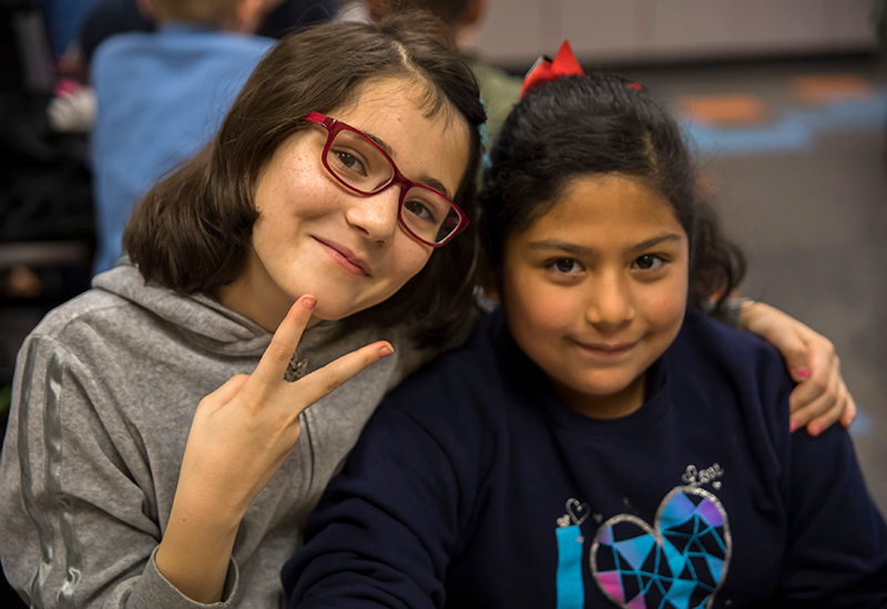 Two students, one showing a peace sign, draping her arm around another student's shoulders
