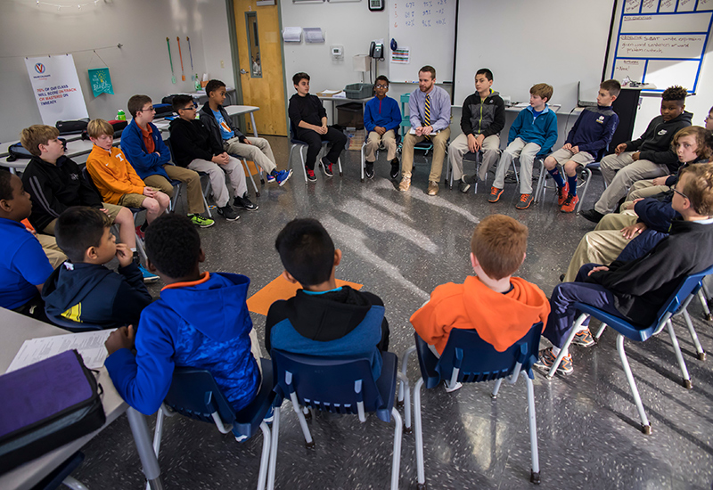 Male students and teacher seated in a circle formation
