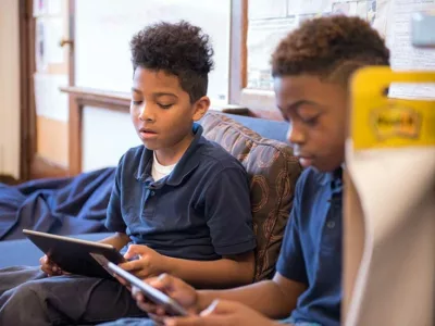 Two students sit on couch, reading from tablets
