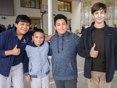 Four students stand in line, two give thumbs up to camera

