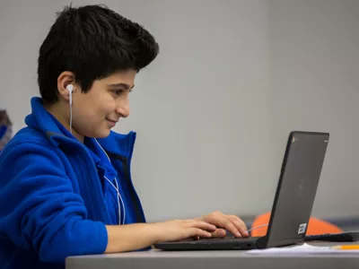 Student wearing earphones smiles as he works on laptop

