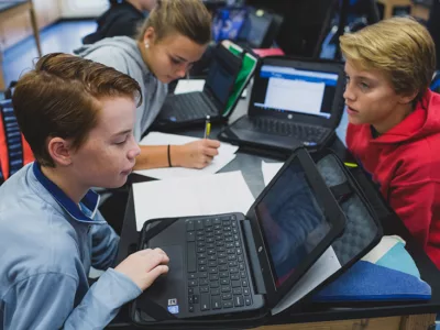 Three students working together while using laptops
