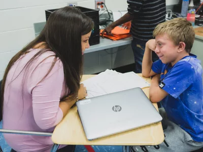 Student speaks with teacher, smiling
