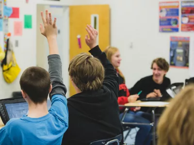 Two students raise their hands while sitting in classroom
