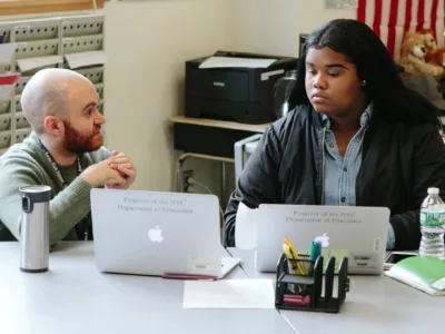 Teacher speaks to student as she looks at laptop
