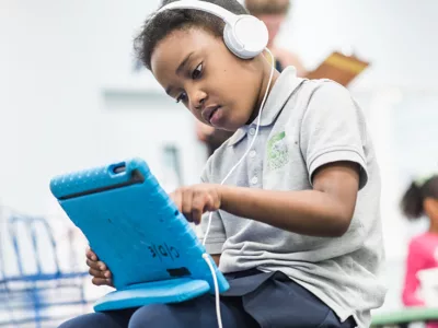 Elementary student looks closely at tablet, wears headphones
