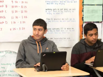 Photo of two students seated with laptops in front
