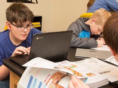 Student looks closely at laptop while other students work around him
