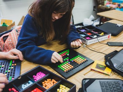 Student works on project, placing colorful blocks in a small grid
