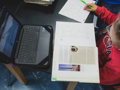 Overhead view of student studying from book, in front of laptop
