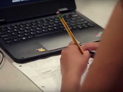 Photo closeup of student working in notebook with laptop on desk
