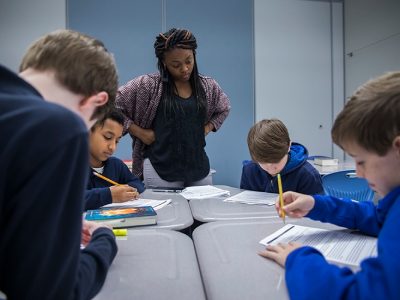 Teacher looks down at table of four students writing
