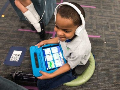 Photo of student seated and working on tablet with headphones

