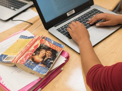 Person types on laptop, set beside a book of Romeo and Juliet
