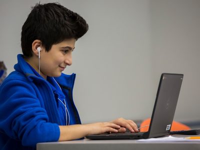 Student wearing earphones smiles as he works on laptop
