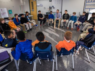 Male students and teacher seated in a circle formation
