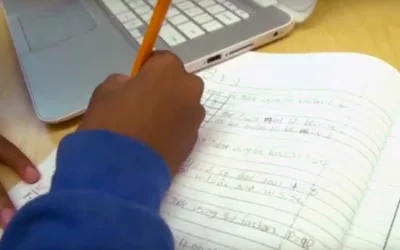 Photo closeup of student working in workbook with device closeby