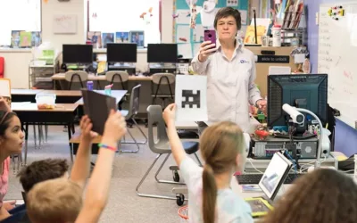 Teacher holds up smartphone in front of students as they raise pieces of paper